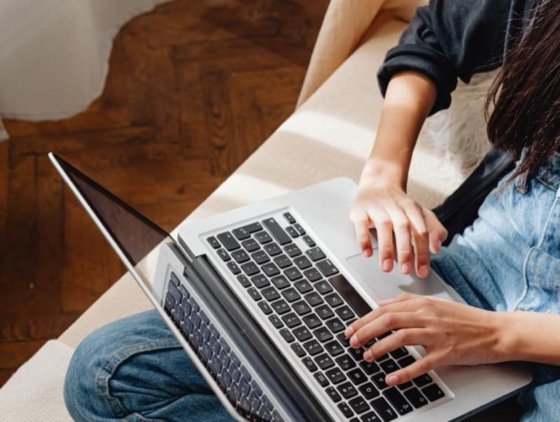 Frau stellt vom Sofa aus am Laptop die Online-Anfrage
